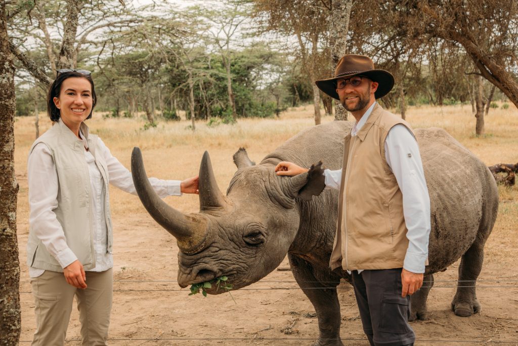 Two people standing next to a blind rhino named Baraka in Ol Pejeta Conservancy.