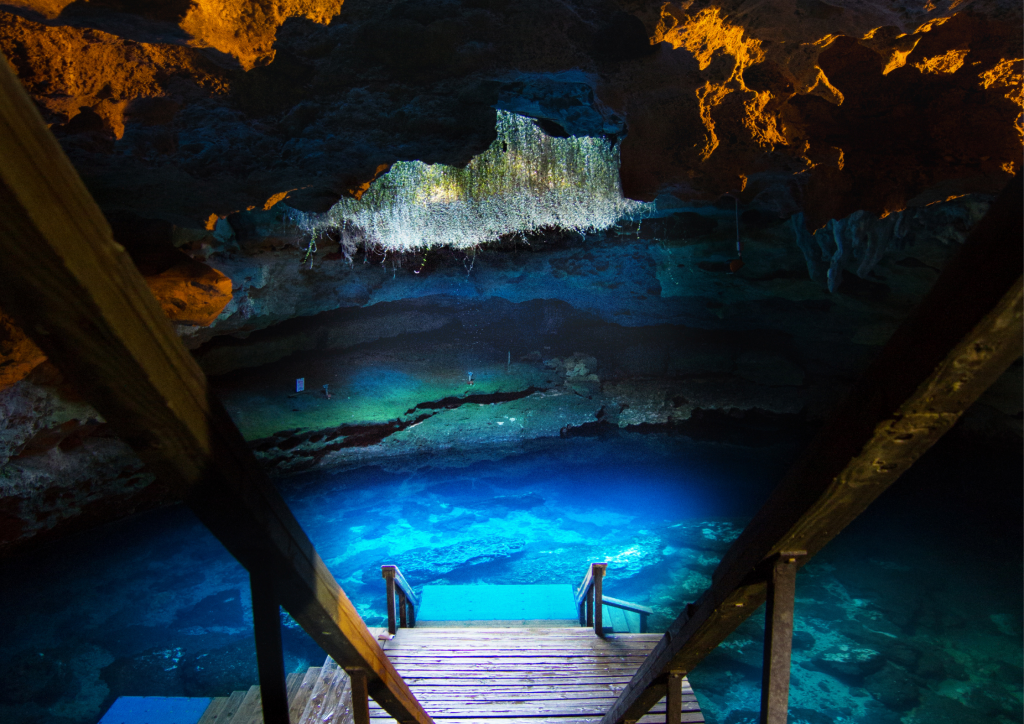 The entrance to a cave with a wooden walkway and bright blue water at the end.