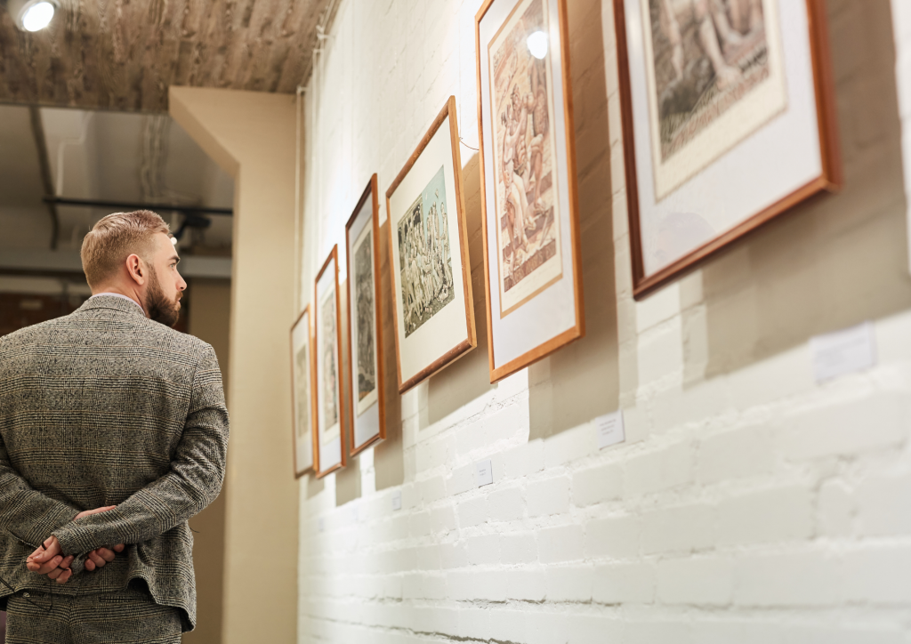 A man in a suit looking at framed pictures in an art gallery.