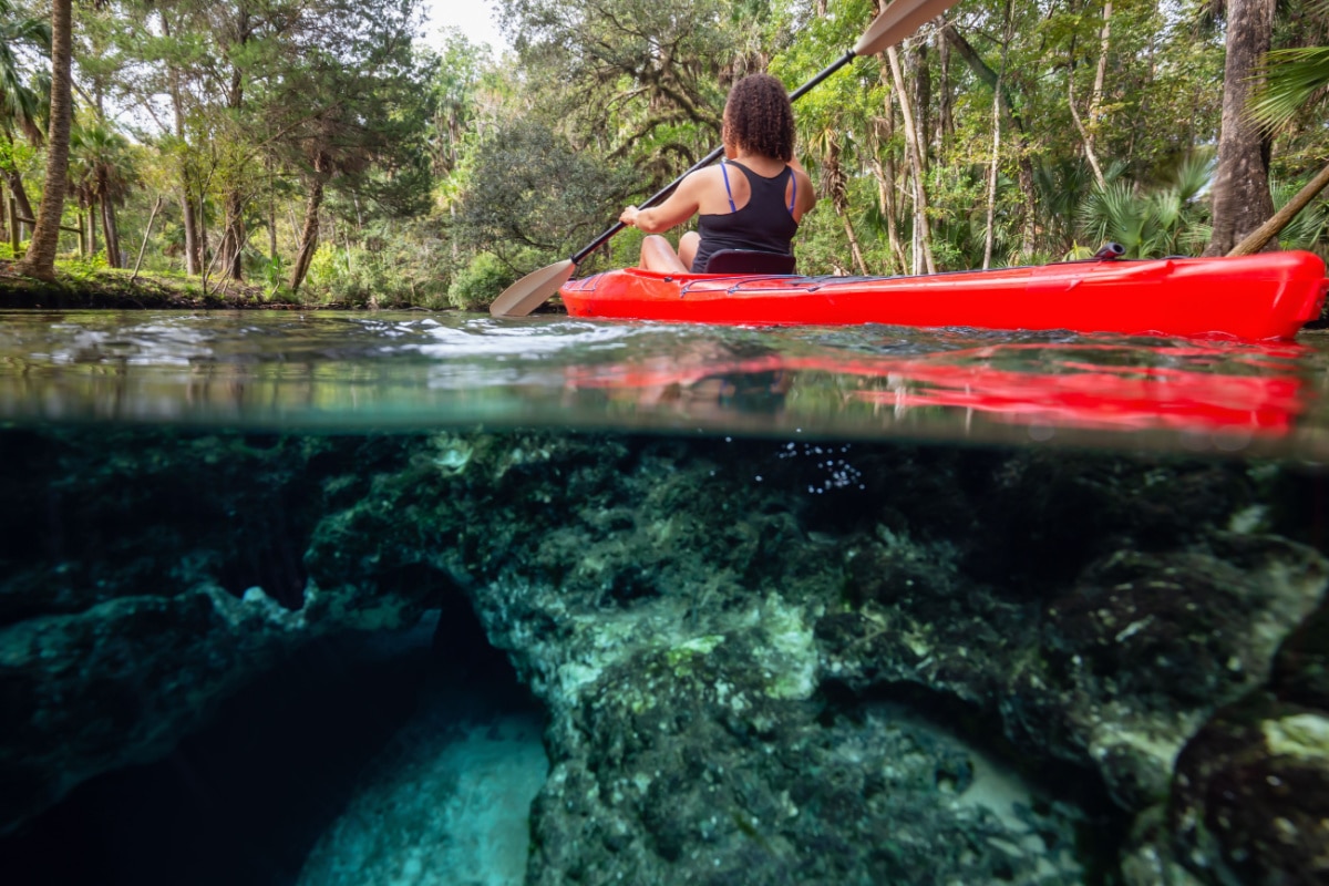 Over and Under picture of a girl kayaking in a lake near an underwater cave formation. Taken in 7 Sisters Springs, Chassahowitzka River, Florida, United States of America.