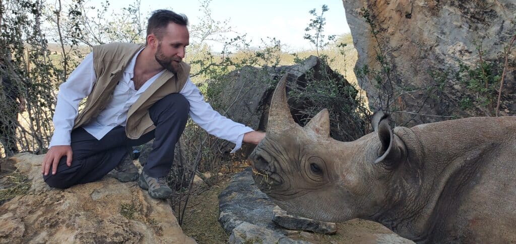 A man petting a rhino on a rock.