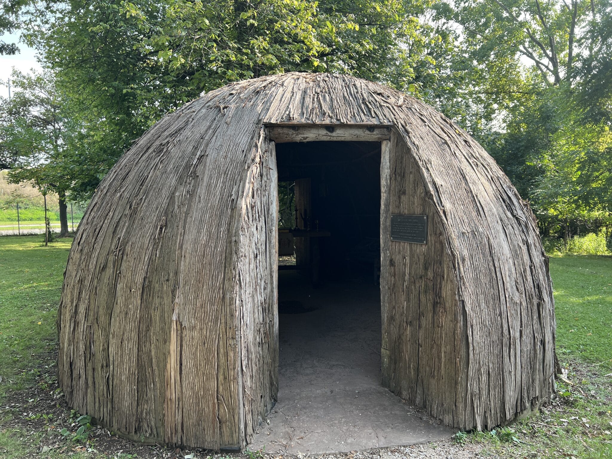 A small, thatched hut features a rounded top and a square door. It shows an early-Wisconsin bark chapel—a replica of Wisconsin’s first Catholic church.