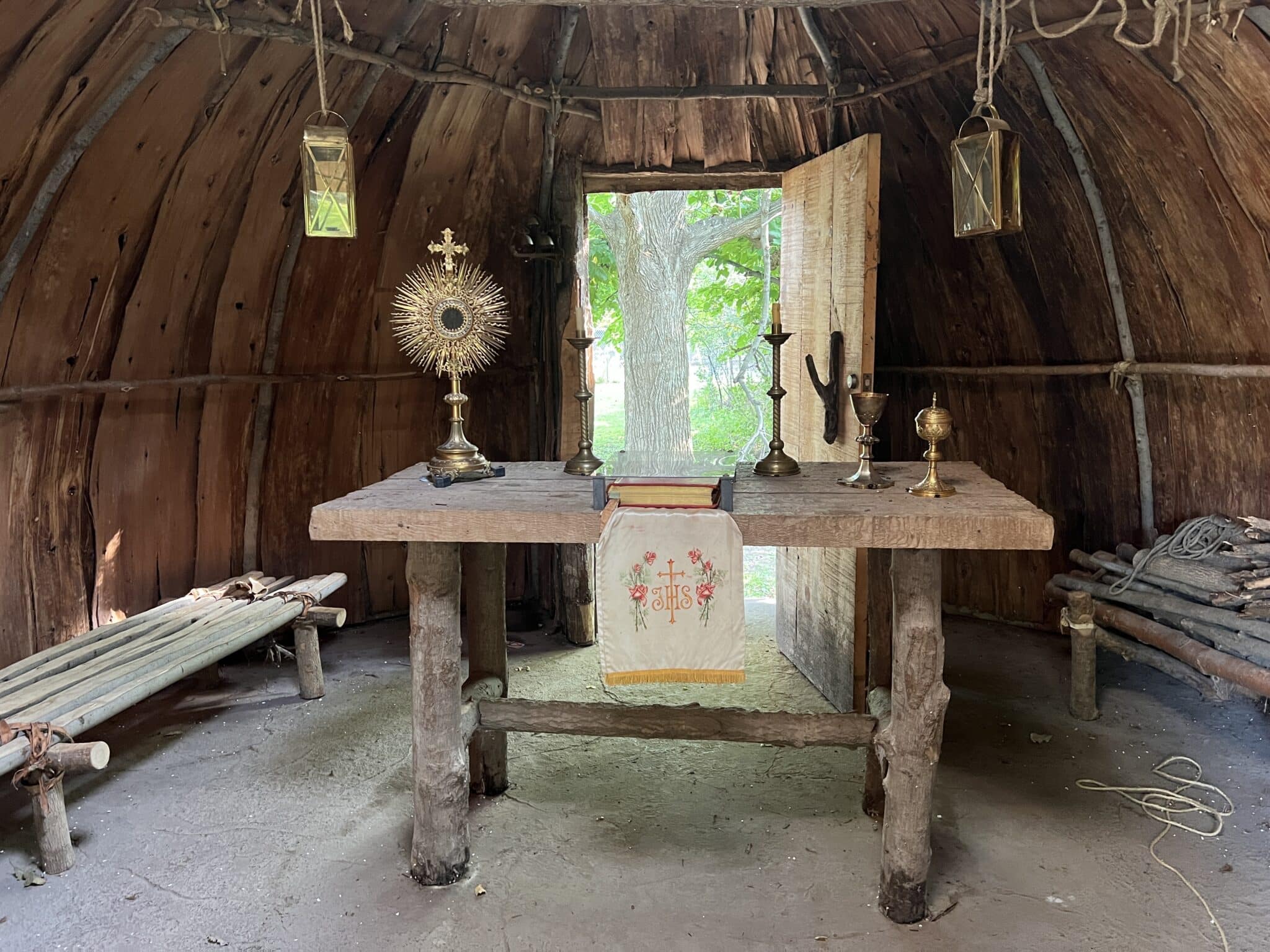 The inside of the bark chapel replica in Green Bay’s Heritage Hill State Park shows how it was decorated for early catholic ceremonies. There is a gold cross along with a communion cup and an embroidered table covering atop a log table. 