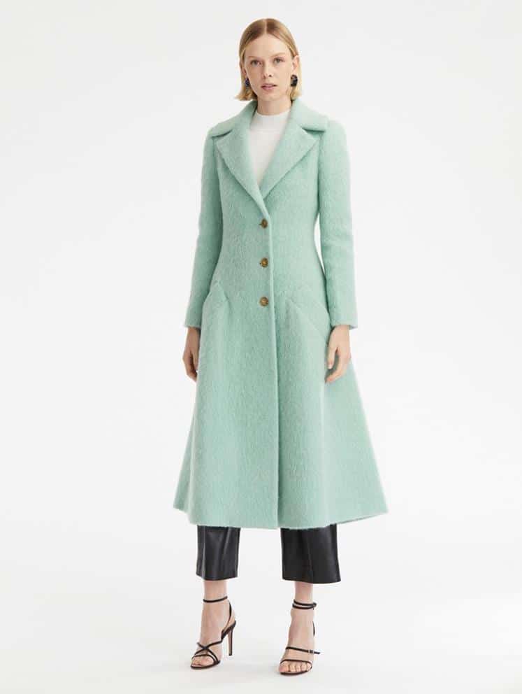 A woman wearing a mint green coat and black pants.