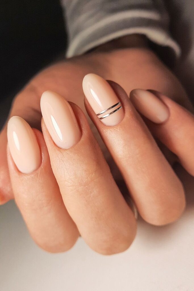 Nude nail color with gold stripe on ring finger.