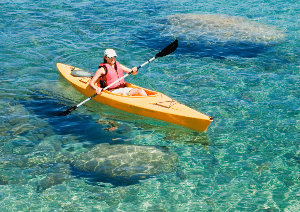 A woman is paddling a yellow kayak in clear blue ocean water.