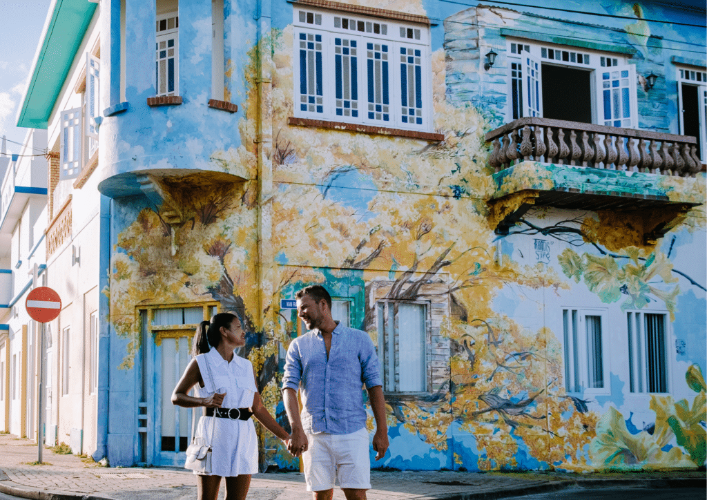 A couple holding hands on the street in Scharloo with street art at the back.