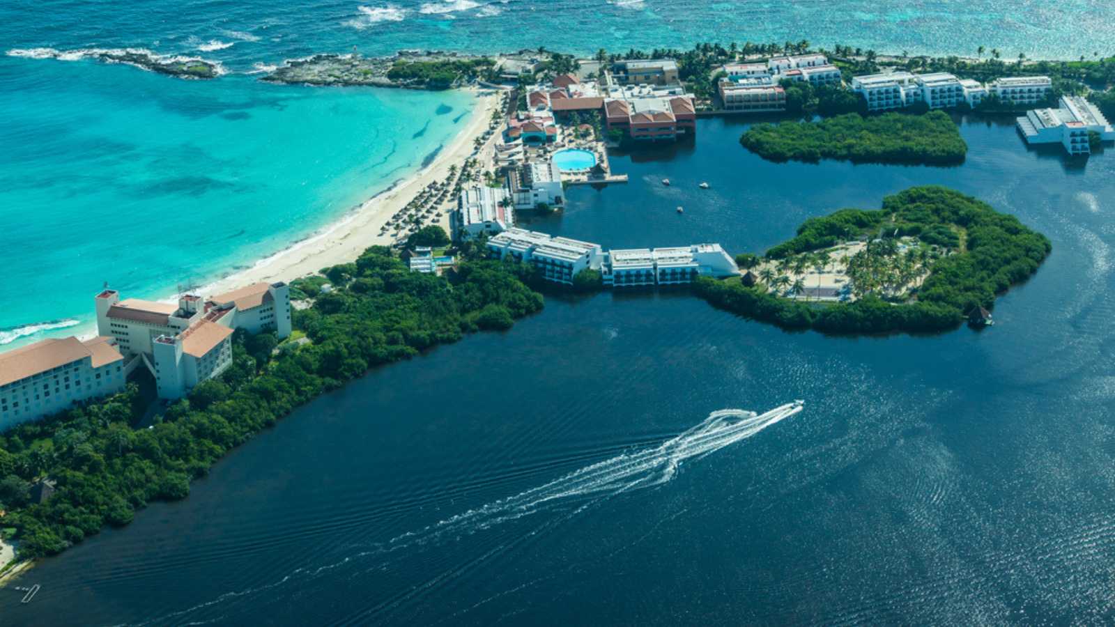 An aerial image of a resort town in Mexico. A strip of land and beaches is surrounded by blue waters. The island is filled with travel resorts.