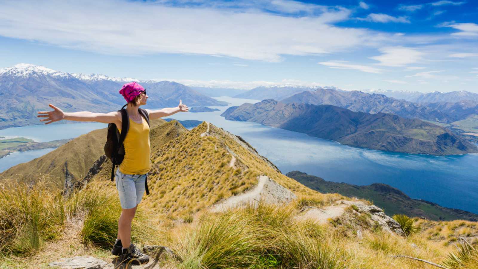 A woman stands at the top of a mountain, overlooking a vast winding river and mountains in the valley.