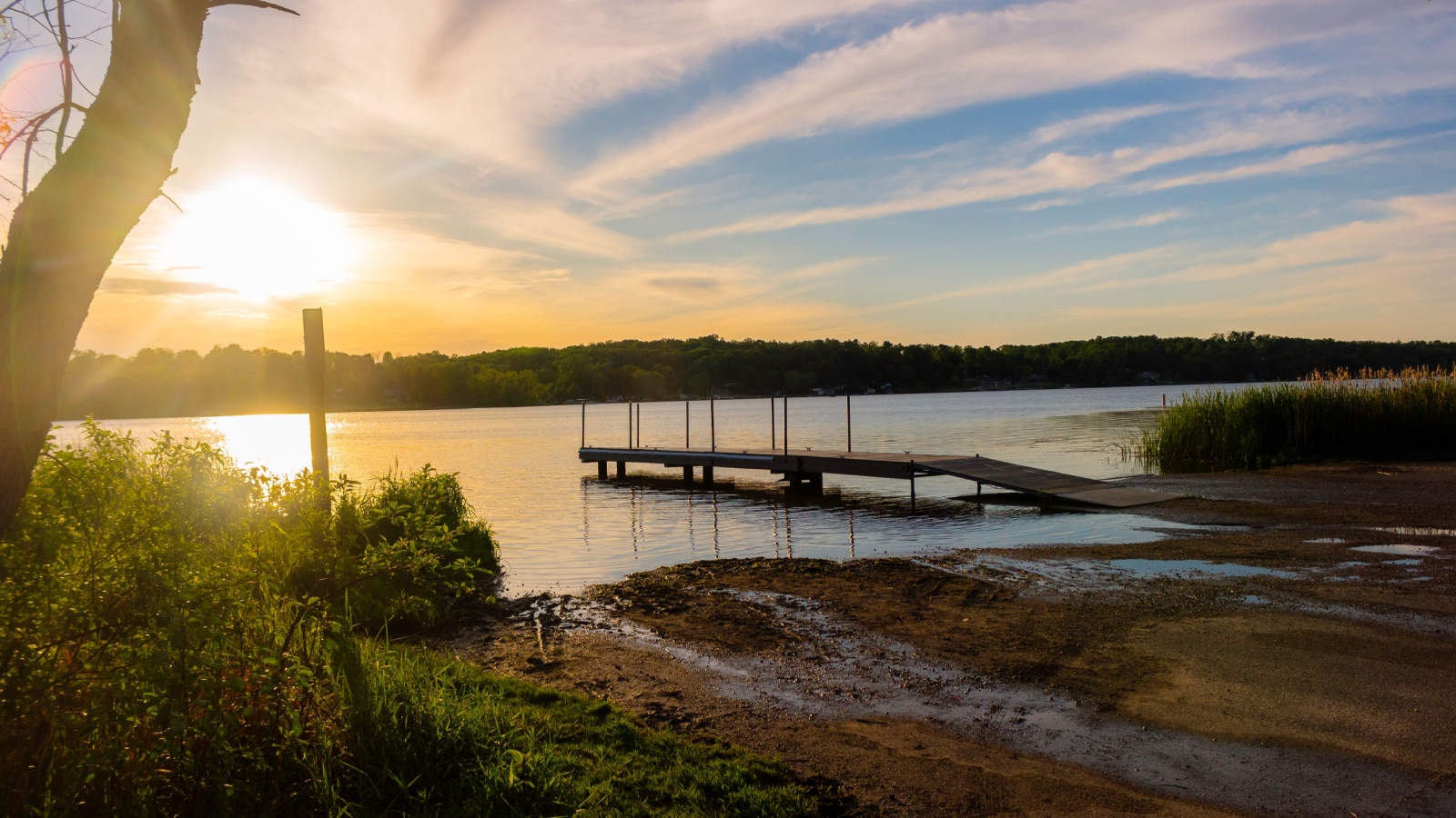 A calm pier at Long Lake Recreation Area in Kettle Moraine State Forest in Kewaskum, Wisconsin, pictured as the sun sets at dusk in a clear sky.