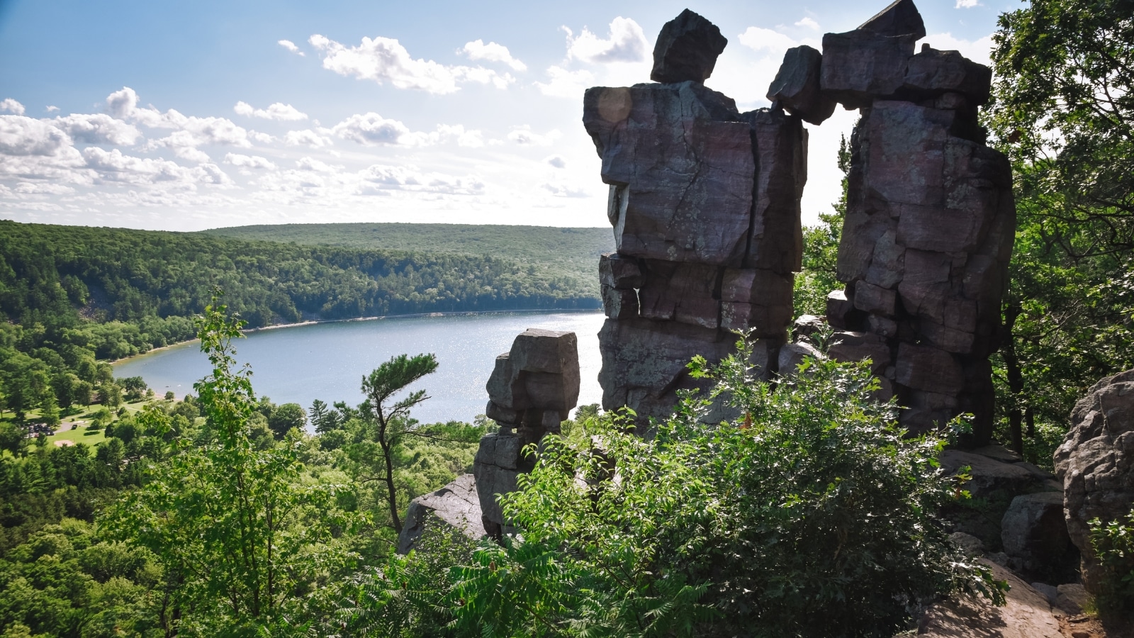 An aerial photo of a towering rock formation in Devil's Lake State Park. In the background is a scenic view of the lake and sprawling forest preserve.