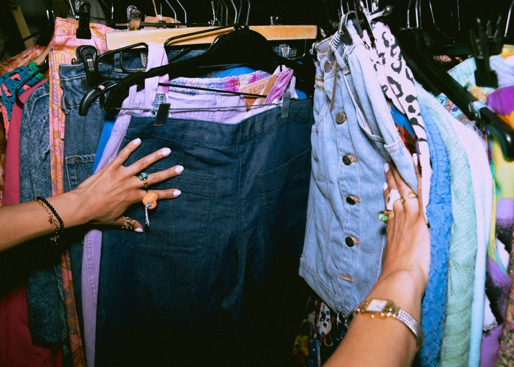 Women shopping for vintage clothing, touching jeans and shirt on a hanger