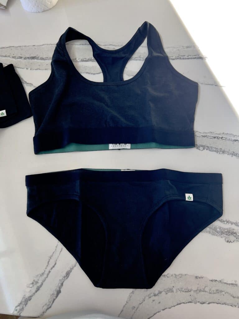 A navy blue matching underwear and sports bra set from the sustainable clothing brand Wama underwear, set out on a white marble counter.