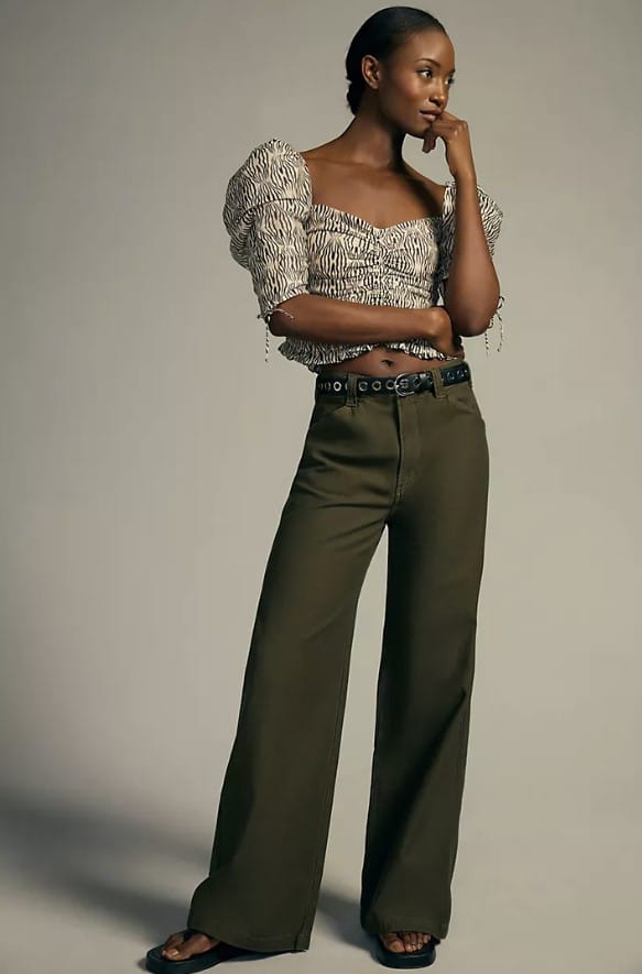 Woman wearing olive green pants and top from Anthropologie posing thoughtfully