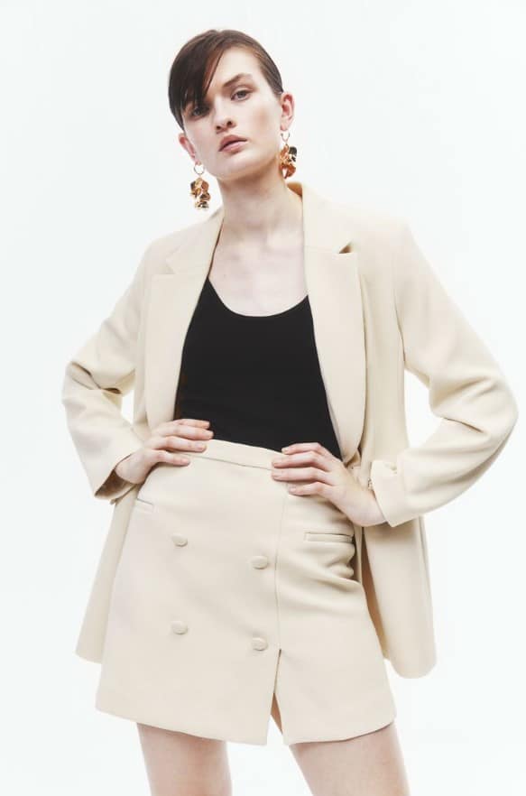 Woman with short hair posing with hand on hips in a cream blazer and shorts from H&M 