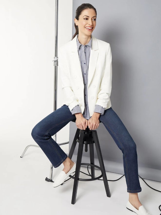 Woman sitting in photo studio on chair wearing a white blazer and jeans from Jones New York