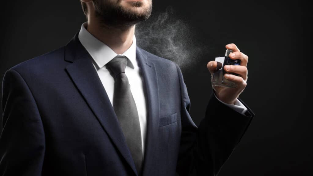 Handsome man in formal suit and with bottle of perfume on dark background.