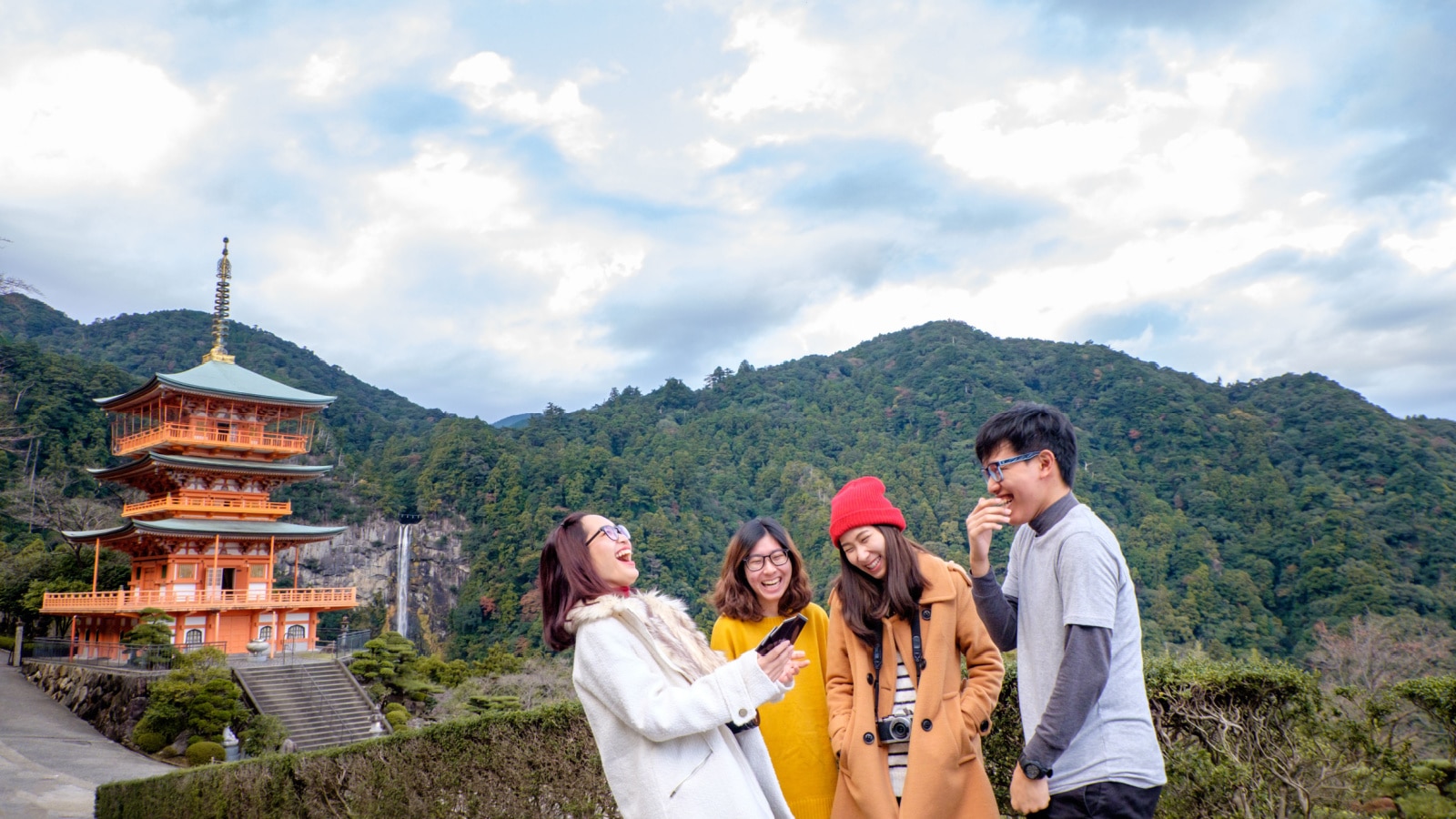 Group of happy tourism gossip and laughing at Sanjunoto Pagoda with background of Nachi waterfalls at Kumano World heritage , wakayama , Japan. Group of young people looking at photo look