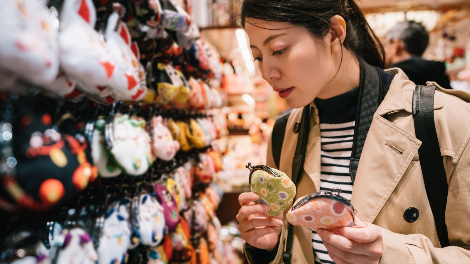 lovely female tourist standing in the souvenir store and choosing coin bags for her friends. traveler buying gifts concept. beautiful girl holding two colorful money purses.