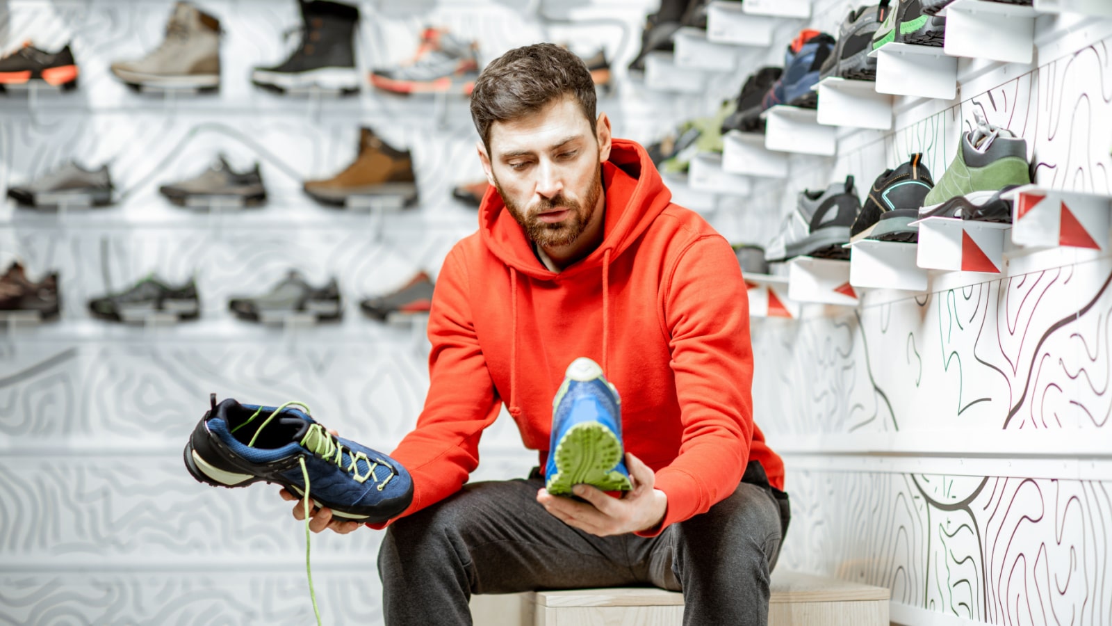 Man choosing trail shoes for hiking sitting in the fitting room of the modern sports shop