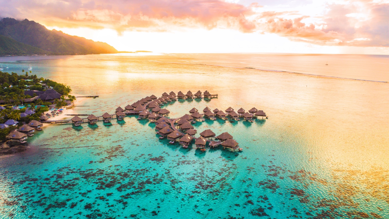 Luxury travel vacation aerial of overwater bungalows resort in coral reef lagoon ocean by beach. View from above at sunset of paradise getaway Moorea, French Polynesia, Tahiti, South Pacific Ocean.