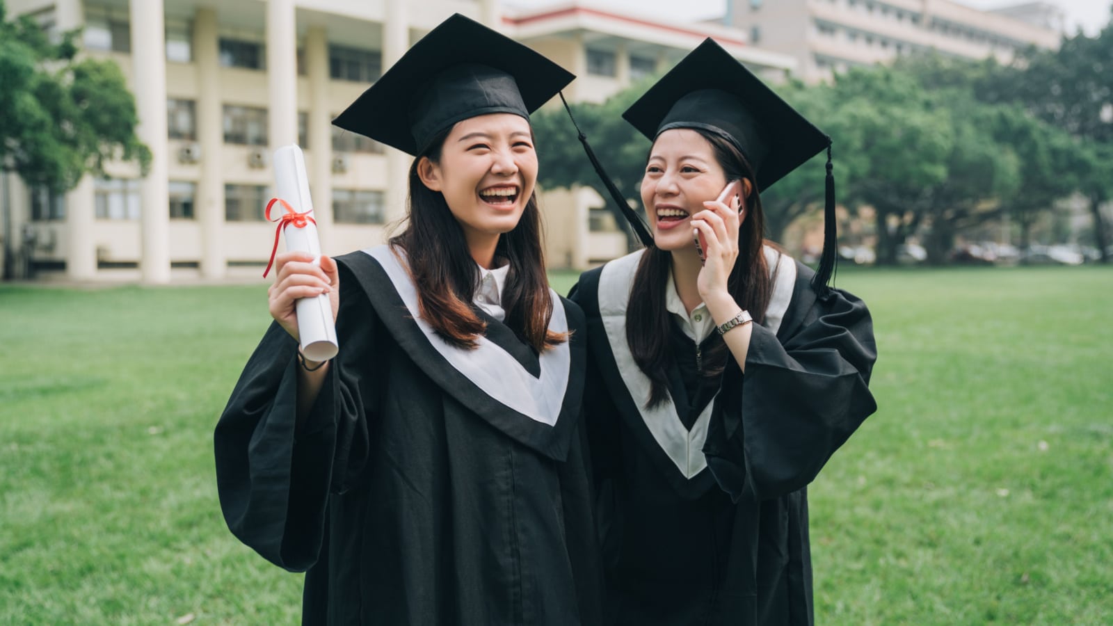 young graduates smiling holding diploma and talking on phone in front of university