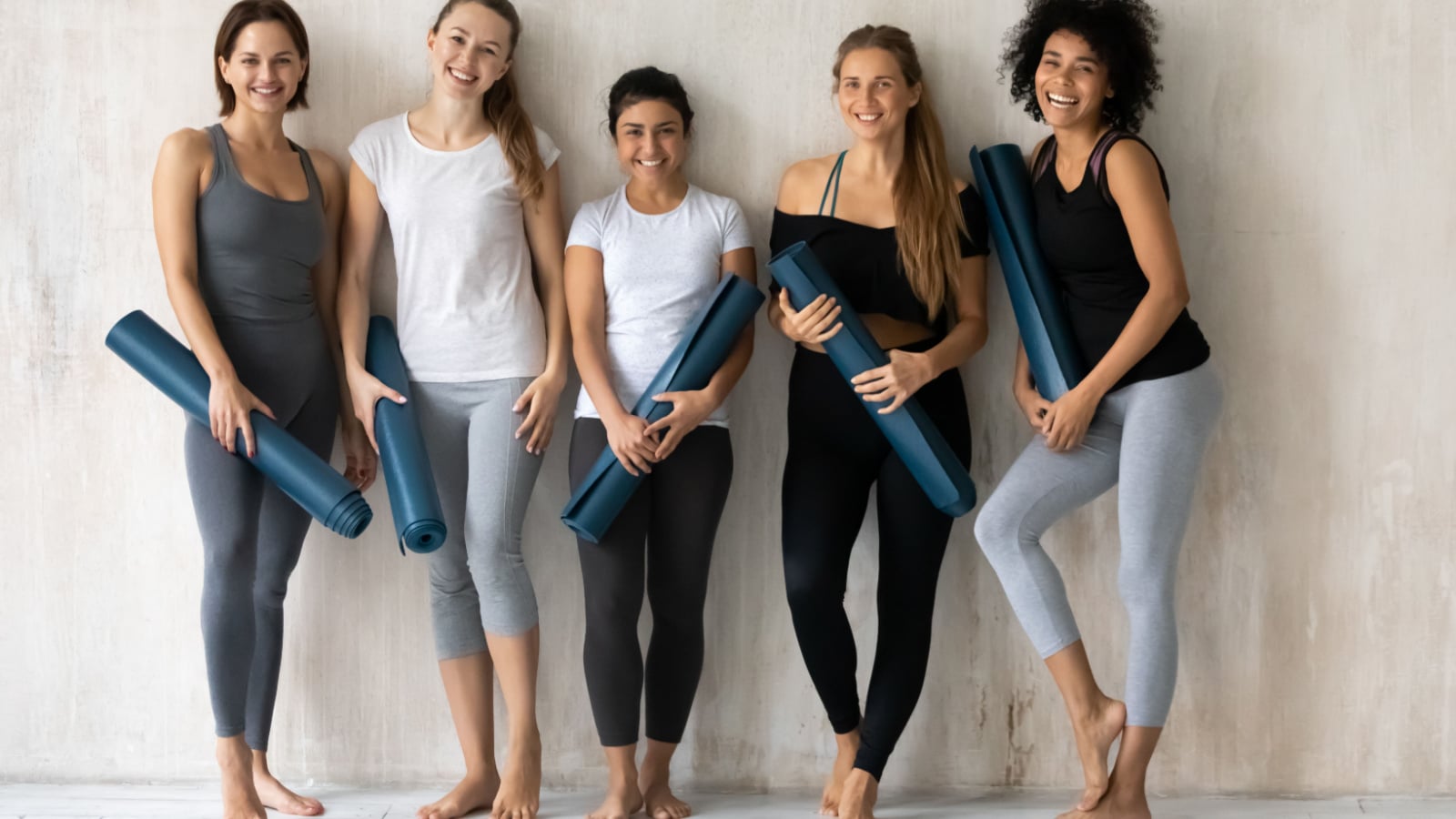 Multicultural millennial students girls holding mats resting after work out posing smiling looking at camera, activewear fashion store advertisement, sport club studio gym instructors portrait concept