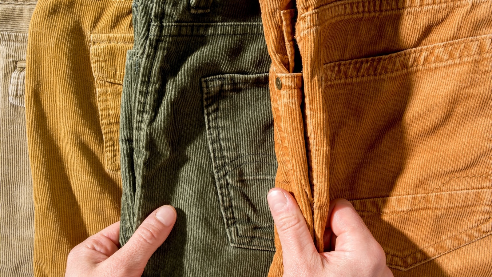 Women hands touch the bright corduroy trousers lying on the counter. Shopping. Top view.