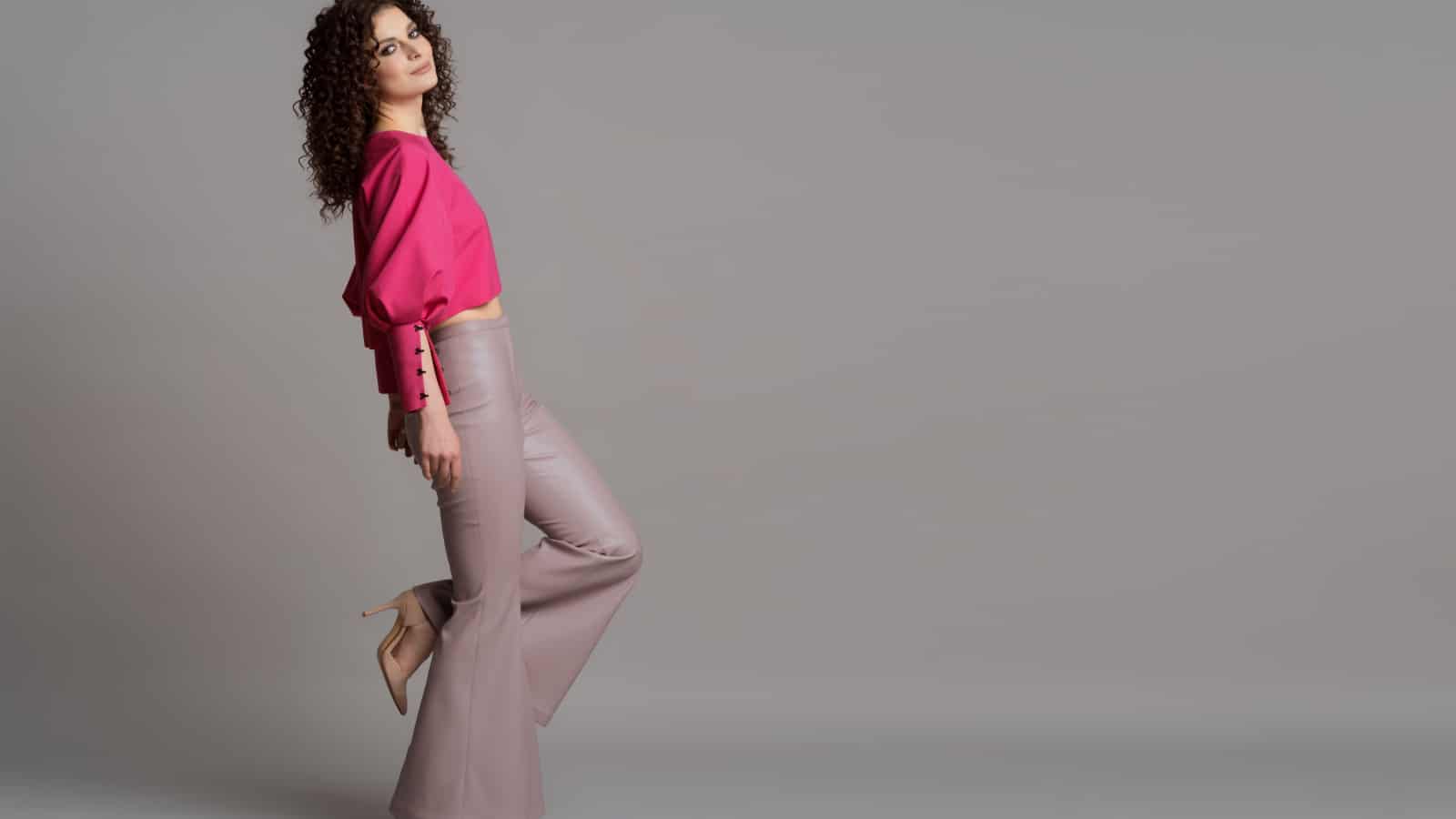 Studio shot of pretty fashion model in pastel purple leather trousers and pink blouse on gray background with copy space