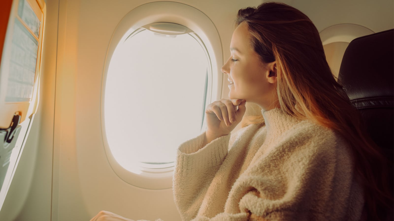 A beautiful girl sits in an airplane at the window and looks at the view. Tourist travel.