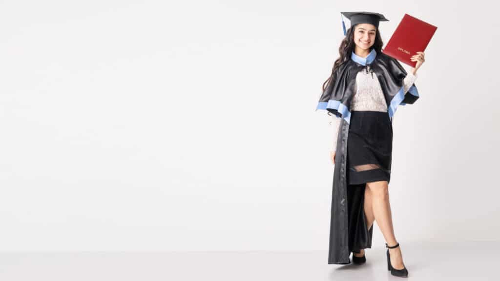 Woman student with diploma on white background with copy space. University graduate indian race woman wearing academic regalia and holding red diploma.