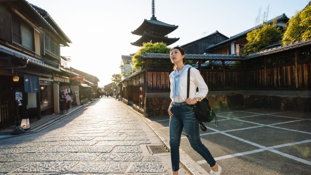 low angle and full length asian girl backpacker is gazing into the distance while wandering around at Yasaka dori near Hokanji Temple in Kyoto, japan at dusk.