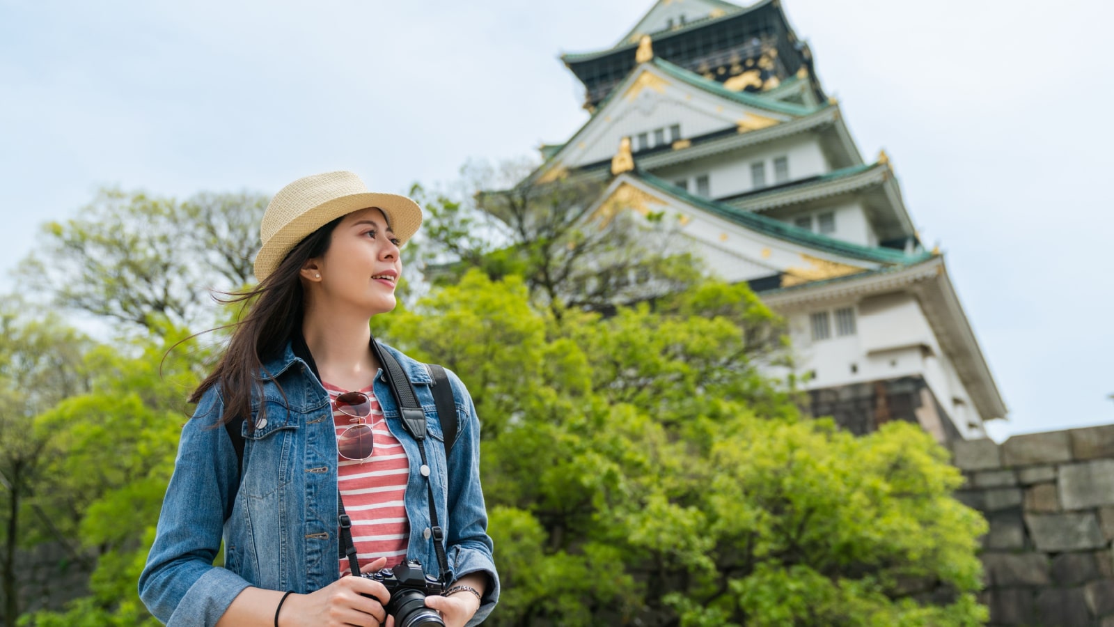 low angle shot portrait of happy asian girl photographer enjoying breeze and looking into distance with magnificent Osaka castle at background in japan