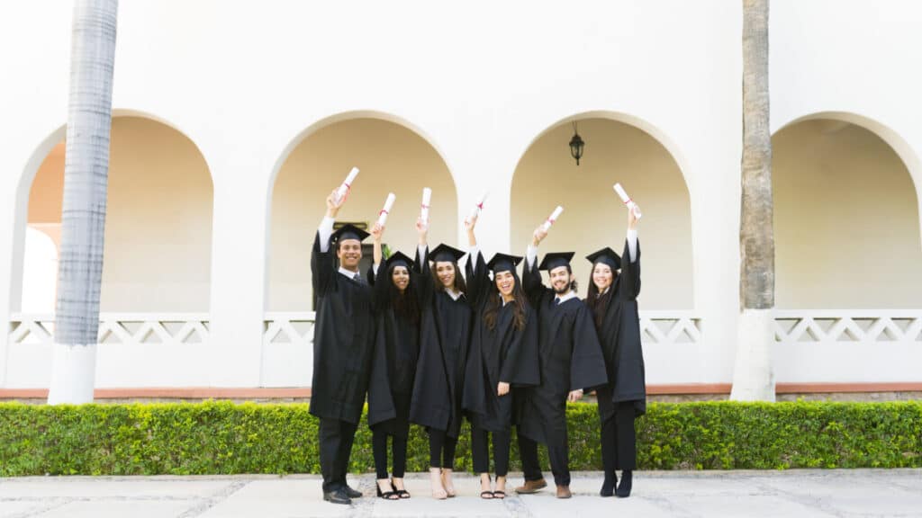 Full length of a group of friends graduates at college campus celebrating after receiving their university diplomas at their graduation