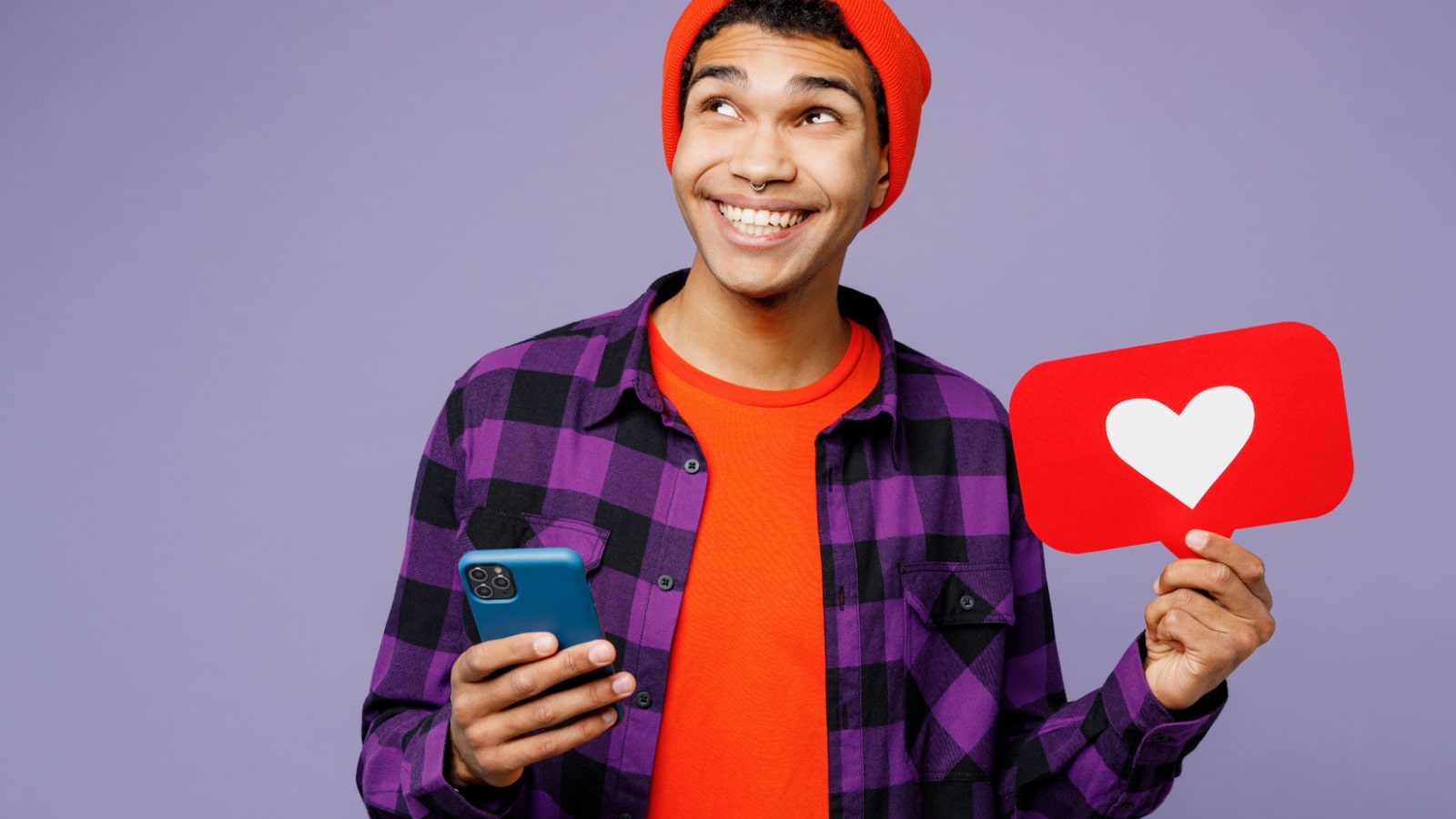 Young man of African American ethnicity wear casual shirt orange hat use mobile cell phone hold heart form like icon sign from social network media feedback isolated on plain purple color background