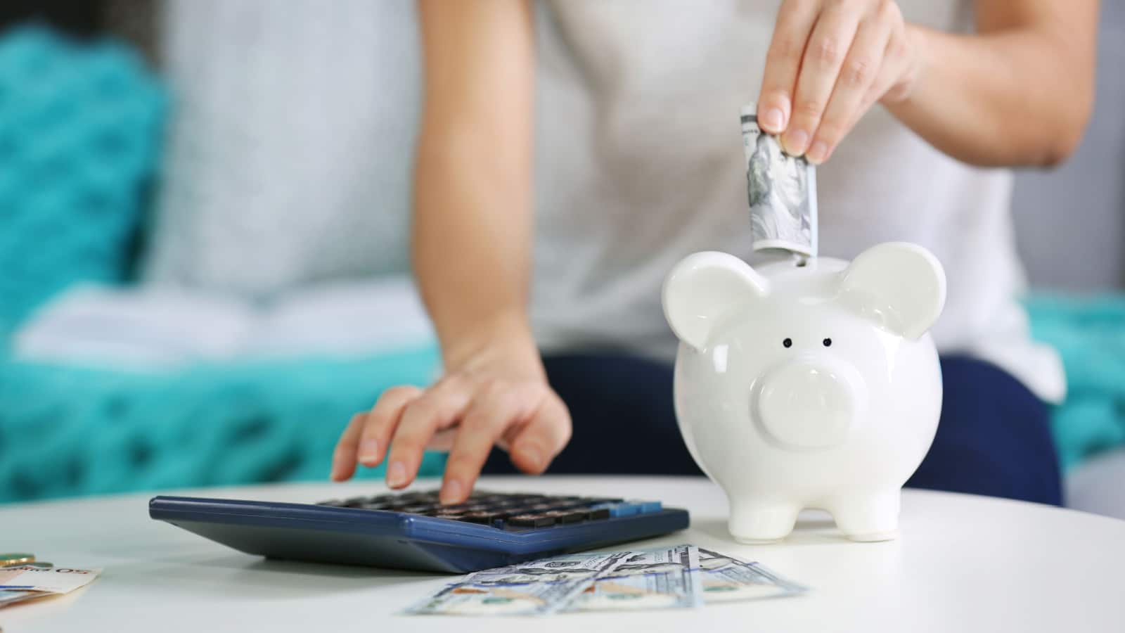 Female hand putting money into piggy bank and counting on calculator closeup / saving money