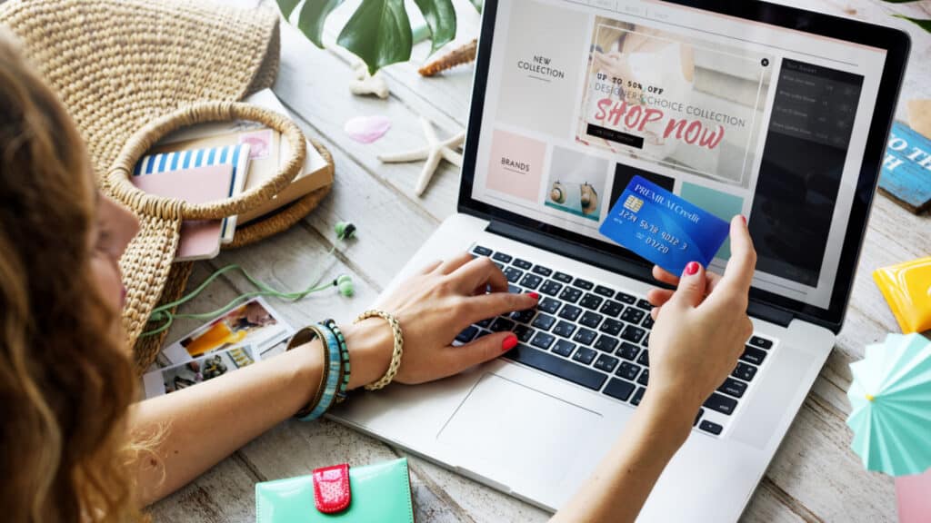 A woman online shopping on her laptop, holding her credit card in her hands.