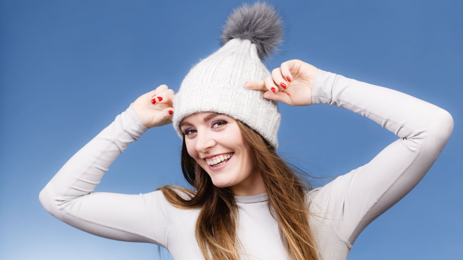 Attractive woman in winter cap and gray sports thermolinen underwear for skiing training studio shot on blue. Long sleeves top