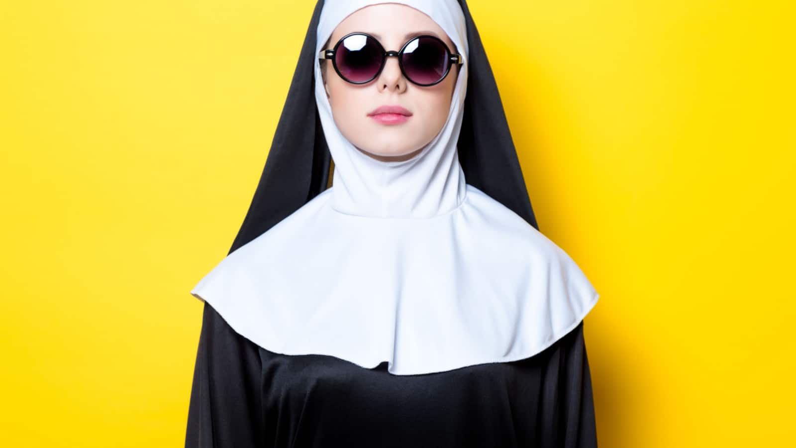 Young nun with sunglasses on yellow background