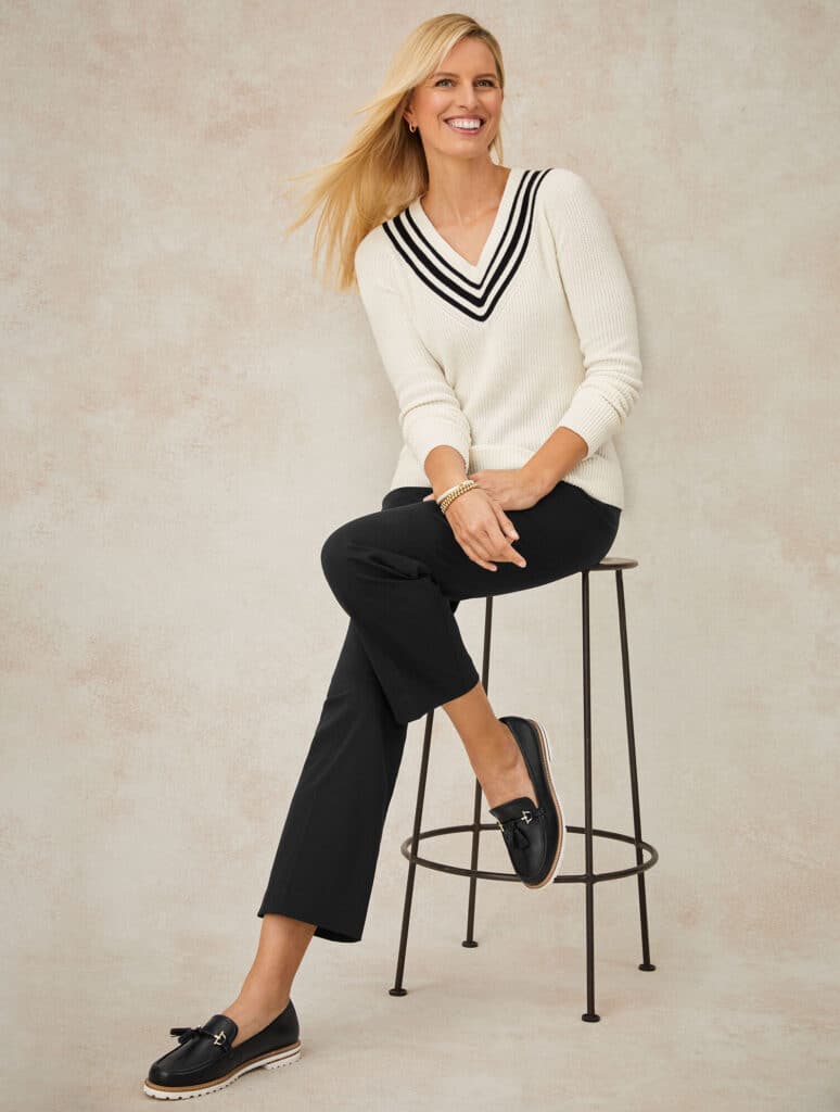Smiling blonde woman wearing a white v neck sweater, plant pants, and loafers from Talbots