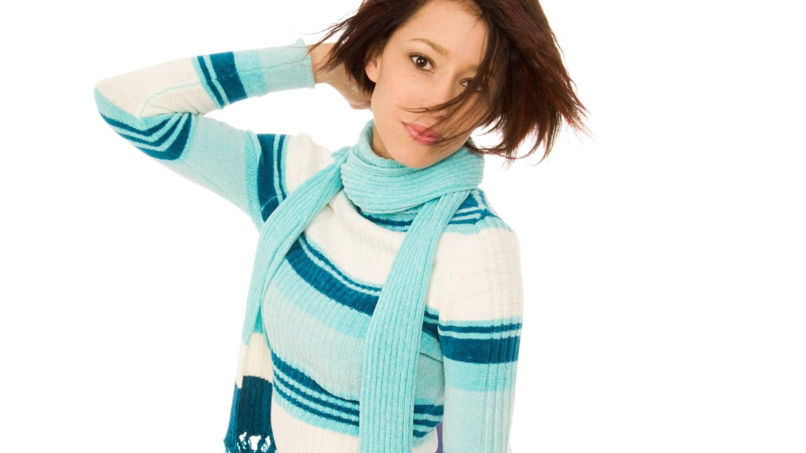 Beautiful young model with blue scarf and wintry sweater, holding a light lavender flowing fabric blowing in the wind.