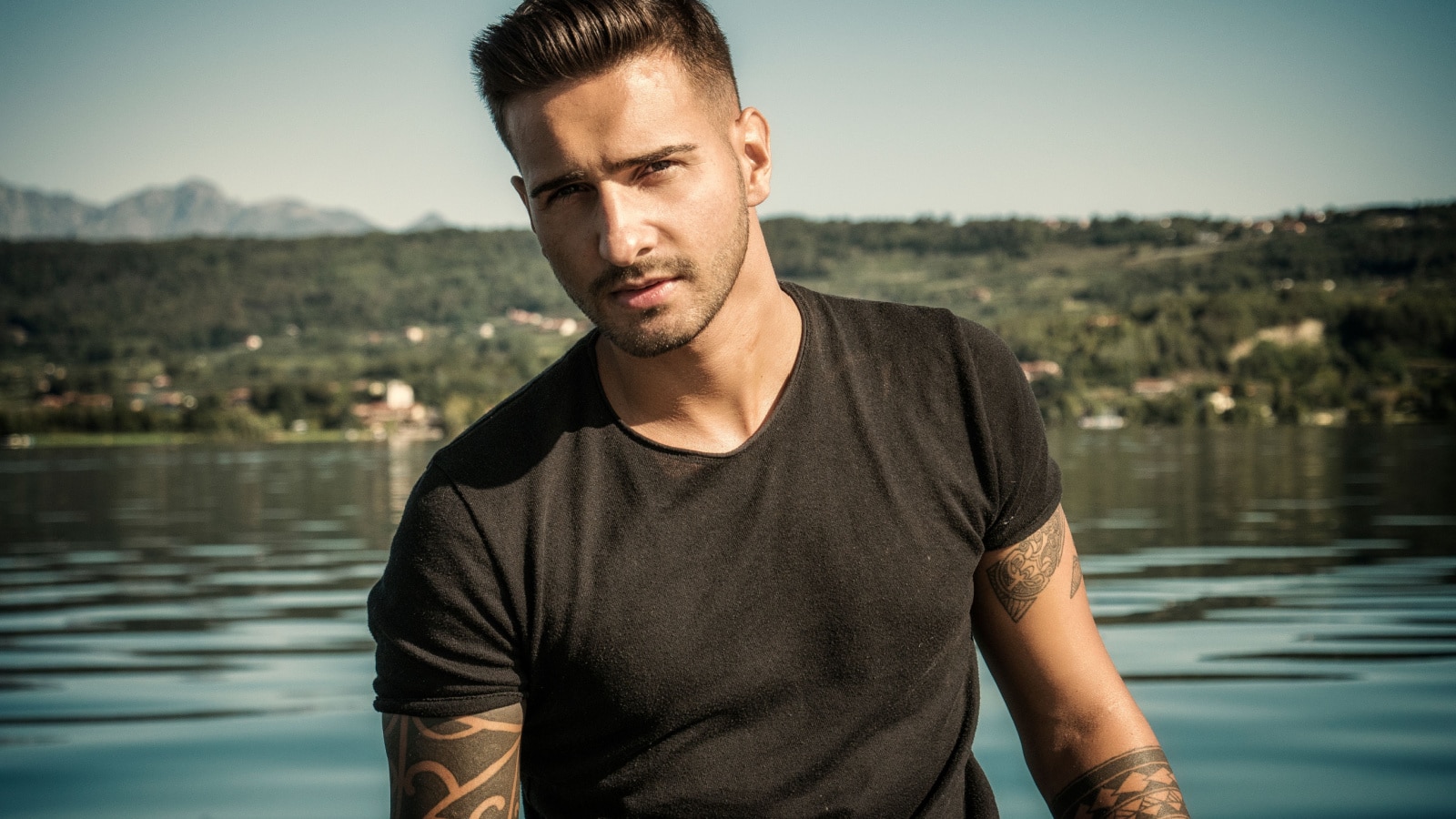 Attractive young athletic man standing in water in sea or lake, wearing black t-shirt
