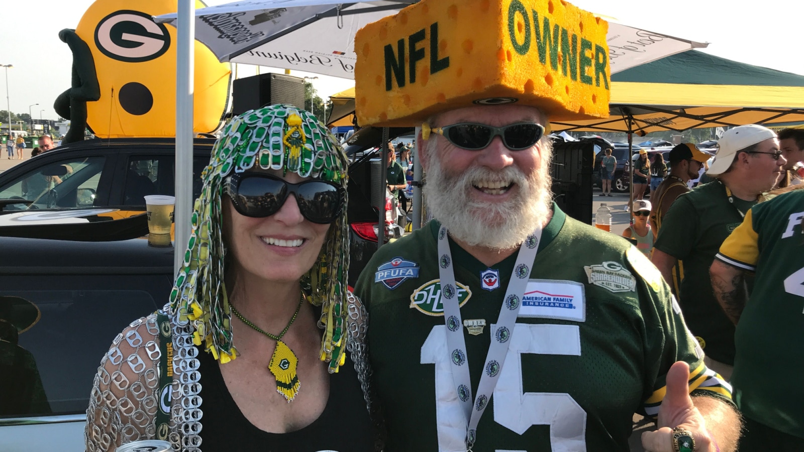 Green Bay, Wisconsin. August 9th, 2018. Packer fans during at tailgate party at Lambeau Field. The man wears a cheesehead that says NFL Owner. The Packers are the only publicly owned NFL team.