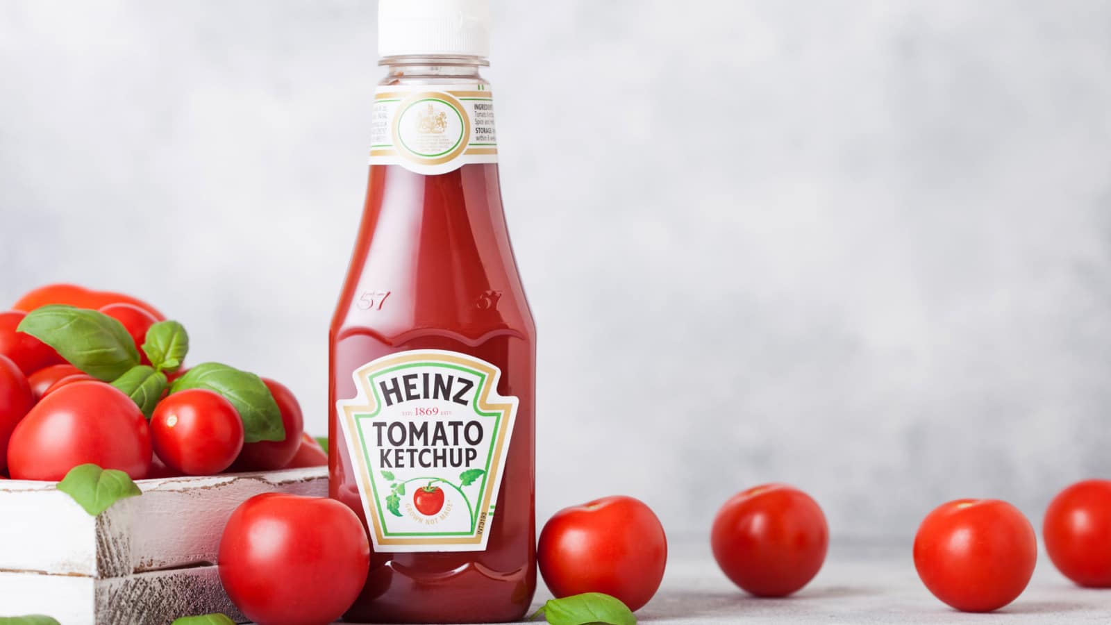 LONDON, UK - SEPTEMBER 13, 2018: Heinz ketchup with fresh raw tomatoes in box on wood background.