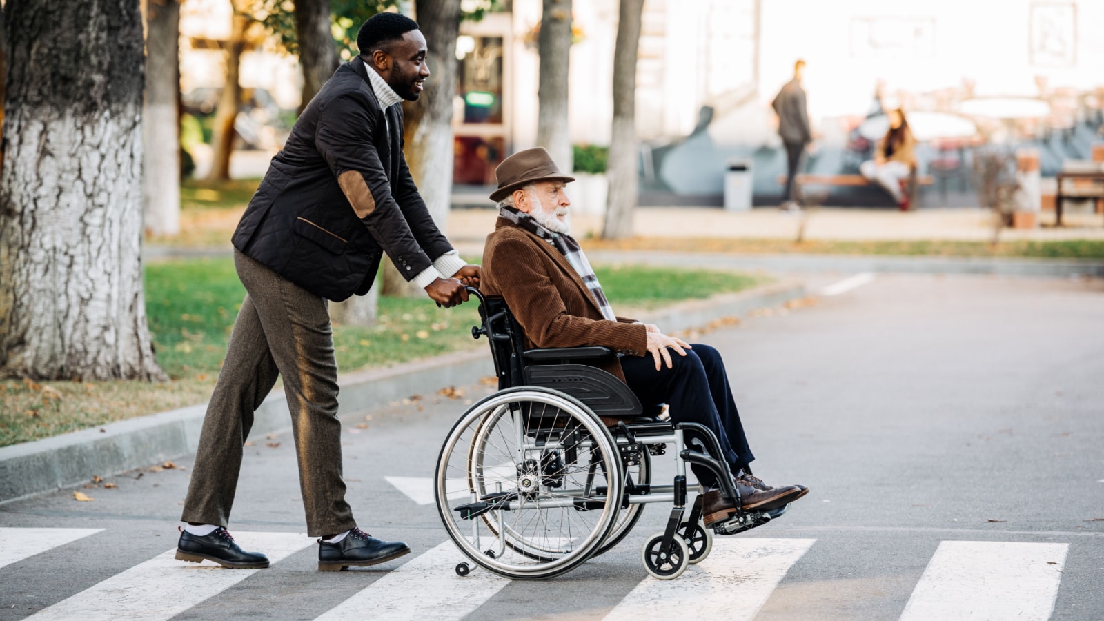 side view of senior disabled man in wheelchair and young african american cuidador riding by street