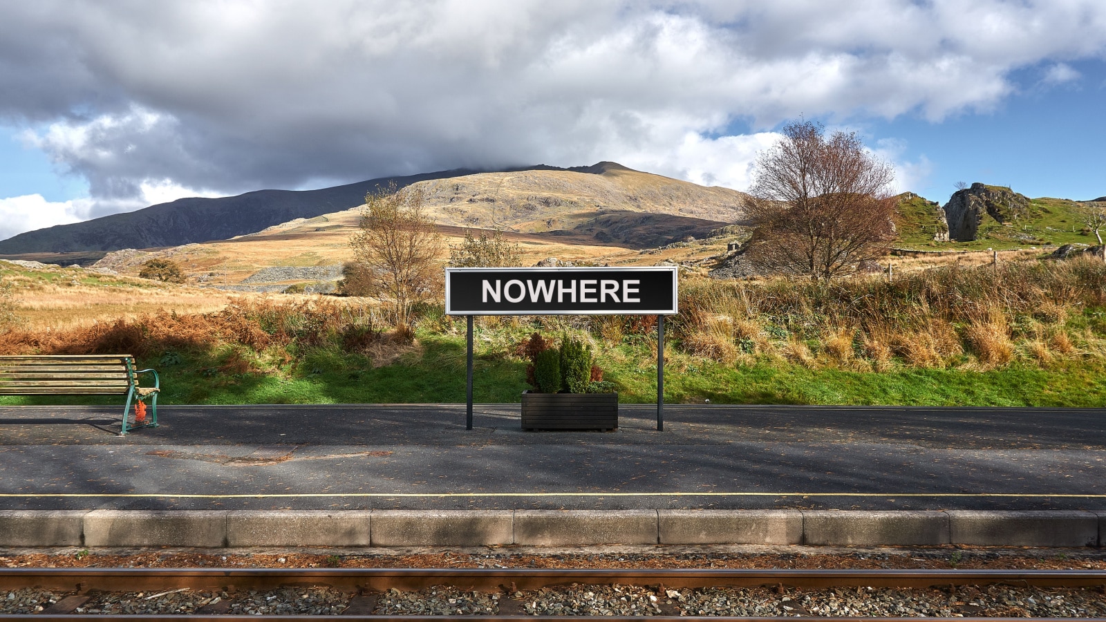 Nowhere descriptive station sign board on platform of remote railway station in rural mountain setting.