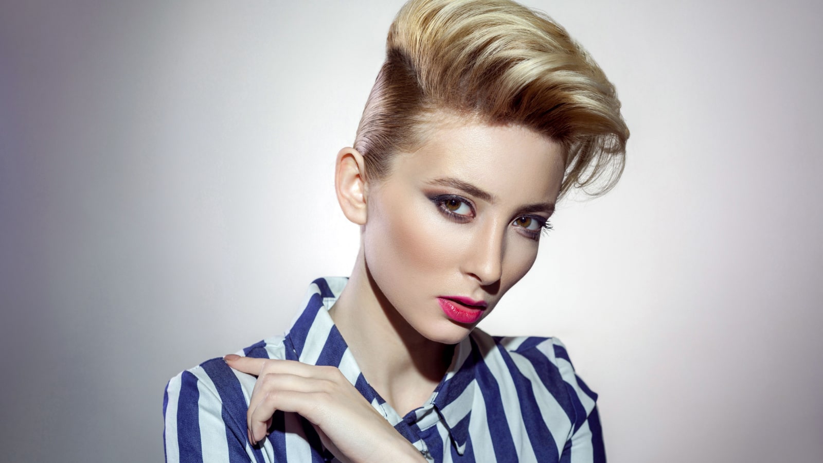 portrait of attractive blonde woman in striped shirt posing on grey background. indoor, studio shot on light grey background.