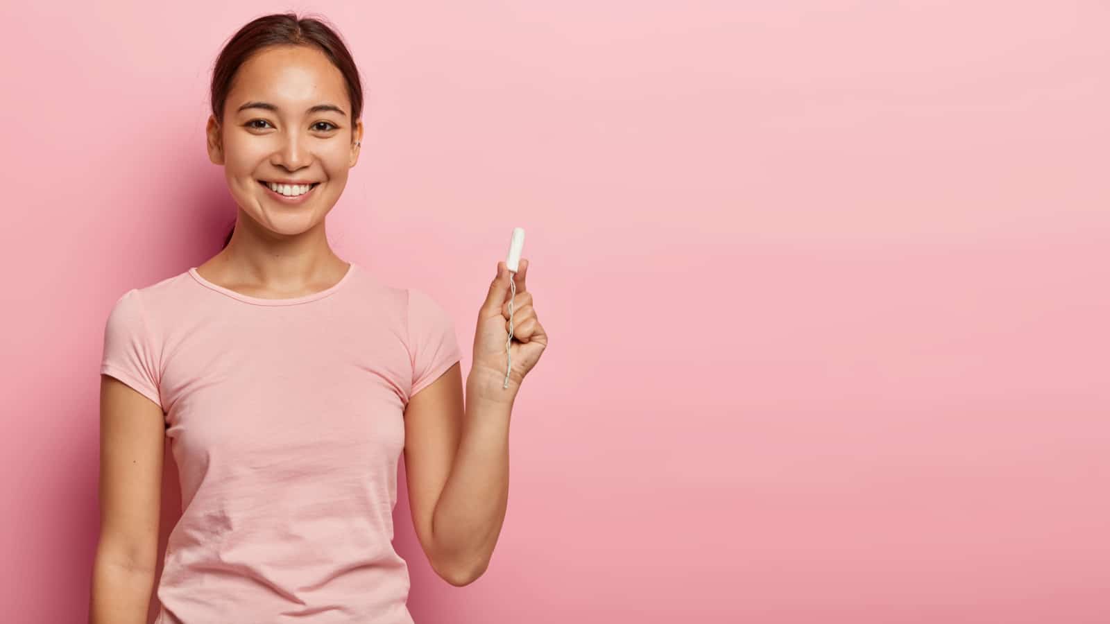 Pretty dark haired female with Asian appearance, holds cotton tampon, cares about hygiene during menstruation, has happy look, dressed in casual outfit. Women, health care, wellbeing concept