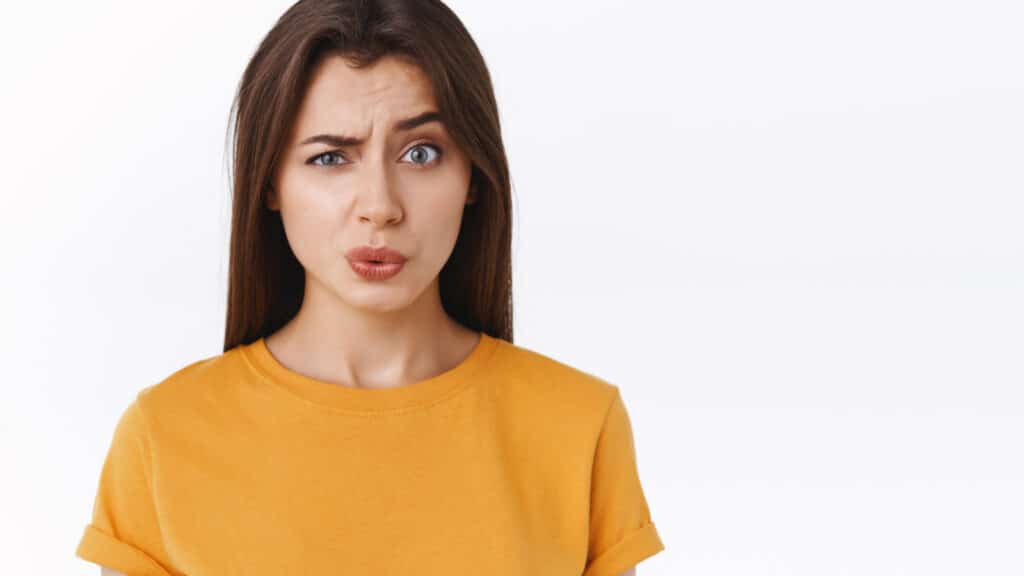 Ouch it probably hurts. Pity good-looking modern brunette woman in yellow t-shirt cringe and grimace as seeing someone got punched in face, folding lips and look uneasy camera, white background