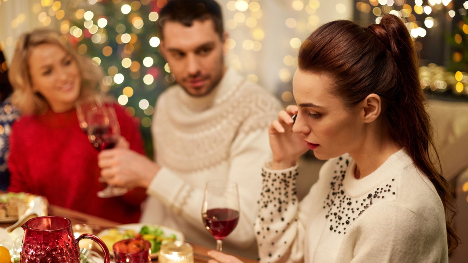 holidays, communication and celebration concept - young woman calling on smartphone and having christmas dinner with friends at home